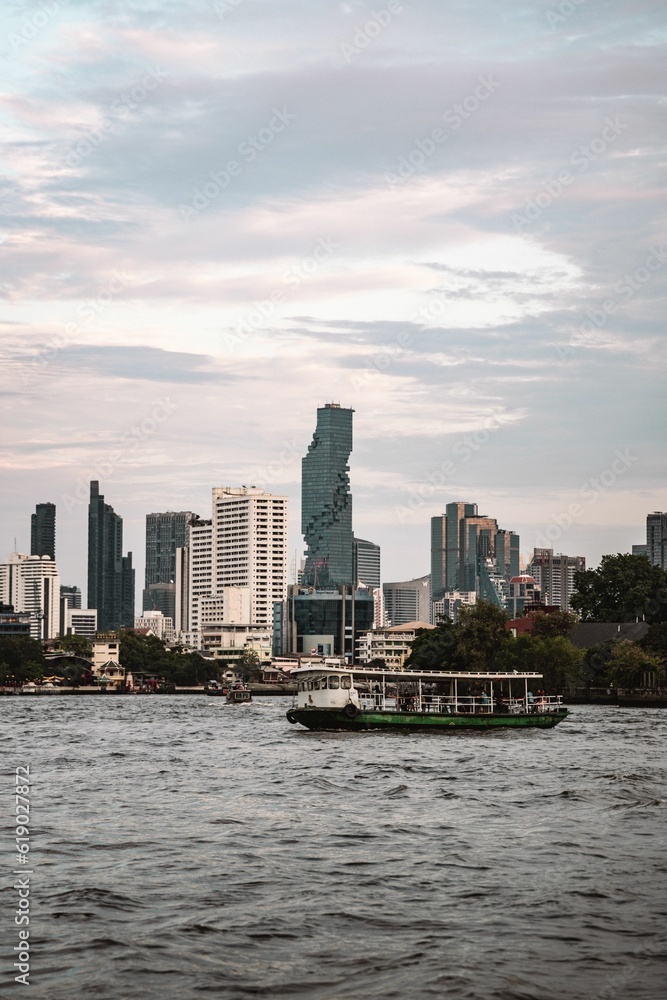Vertical shot of a beautiful modern cityscape with a boat in the foreground in Bangkok, Thailand