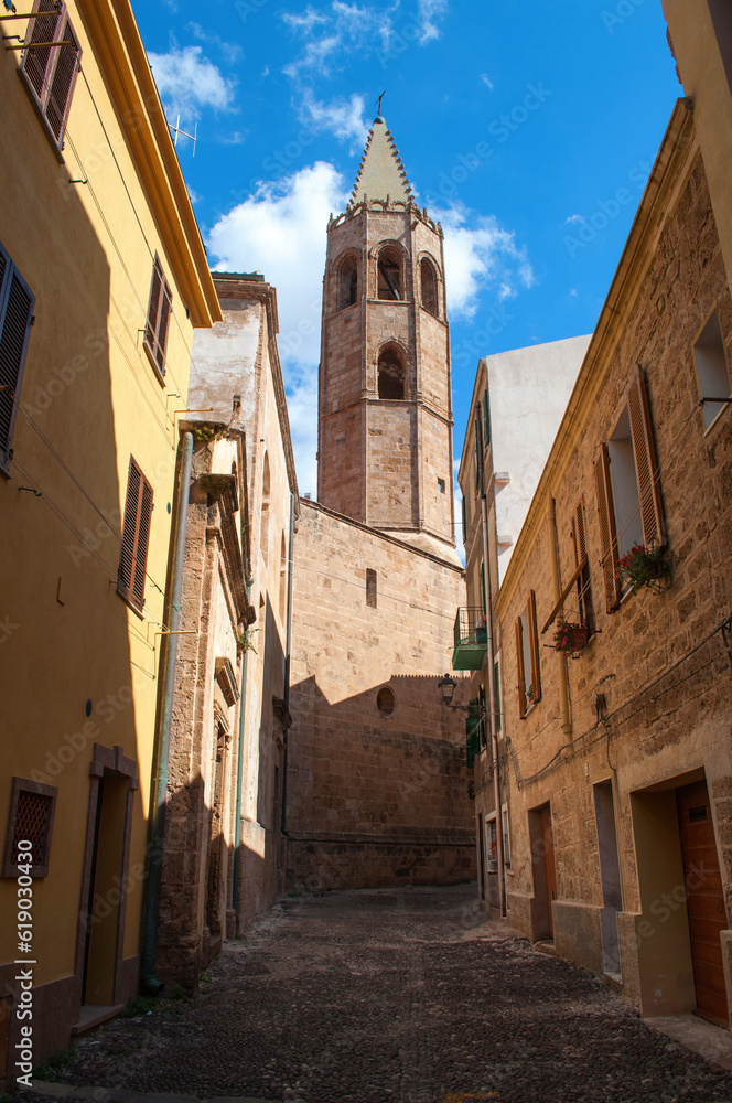 Old street with church tower and stone houses in Alghero city on Sardinia island, Italy.