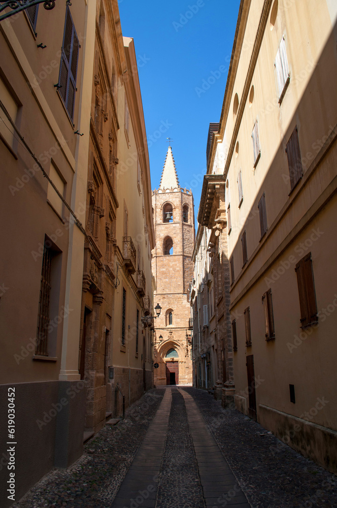 Old street with church tower and stone houses in Alghero city on Sardinia island, Italy.