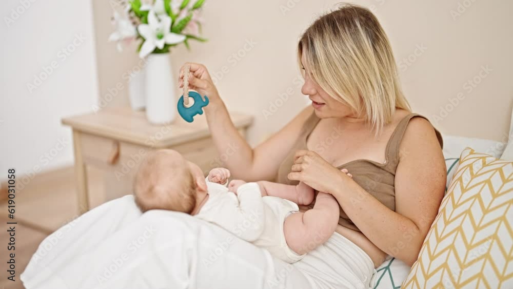 Mother and daughter sitting on bed together playing with ratlle at bedroom