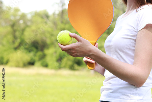 Play paddleball with a wooden racket on the background of nature. A wooden paddle for playing tennis and a ball in the hands of a girl. Outdoor games. Close-up © Mariia
