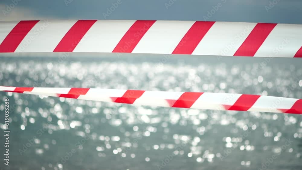 Red white warning tape barrier ribbon swinging in the wind across exotic sea beach background without people. No entry Red White caution tape. No holiday concept, delayed travel, no summer plans Red white warning tape barrier ribbon swinging in the wind across exotic sea beach background without people. No entry Red White caution tape. No holiday concept, delayed travel, no summer plans