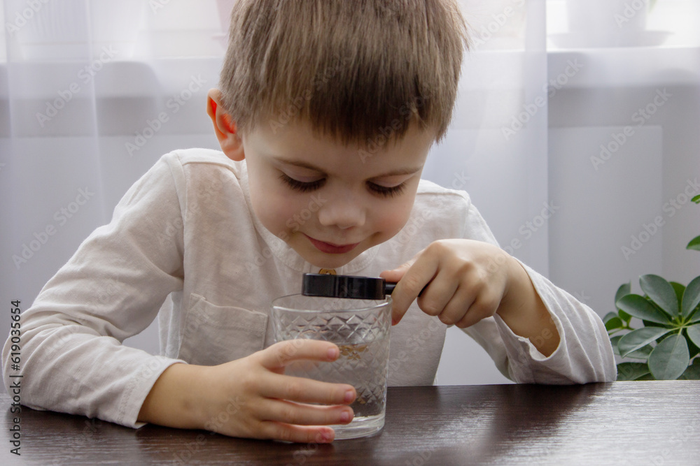 the child looks at the water through a magnifying glass. Selective focus.