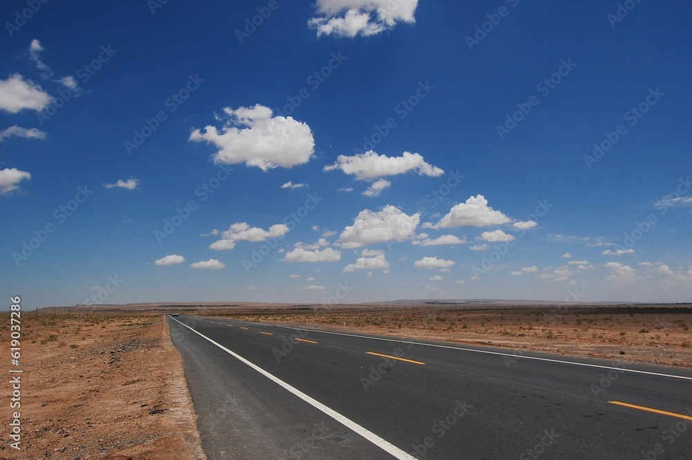 Isolated desert highway stretching out into the horizon, surrounded by lush clouds Isolated desert highway stretching out into the horizon, surrounded by lush clouds