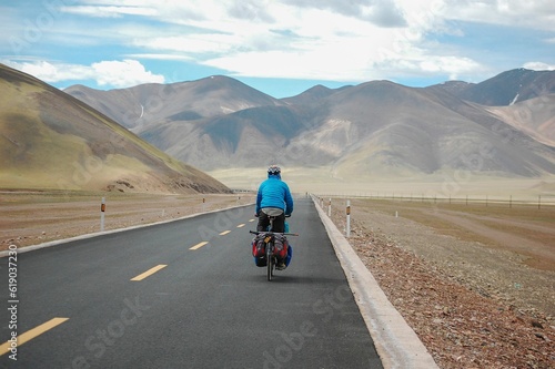 Hiker riding a bicycle on a rural road surrounded by beautiful mountainous scenery