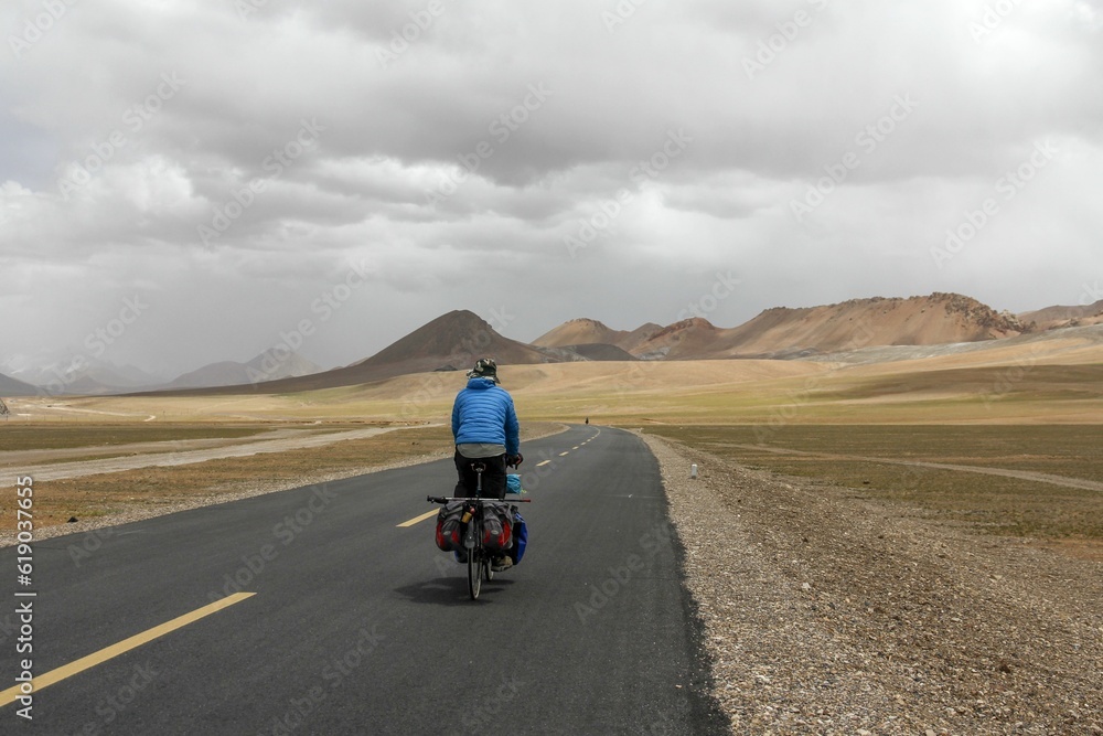 Human riding bicycle on road through desert surrounded by mountains Human riding bicycle on road through desert surrounded by mountains