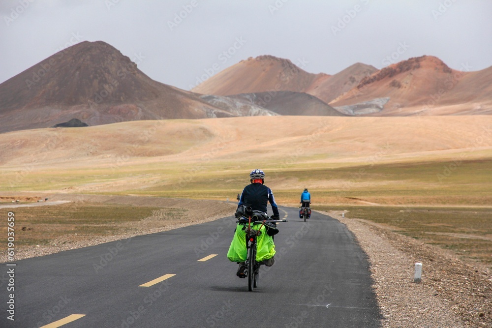 Human riding bicycle on road through desert surrounded by mountains