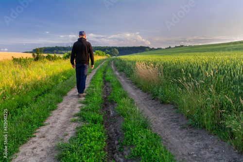 A man in a black hooded sweatshirt walks along a country road between fields