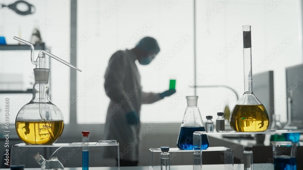 Laboratory of modern medical research. A male scientist analyzes a green liquid in a flask. Blurred background. Advanced scientific laboratory of medicine, biotechnology, molecular biology. Laboratory of modern medical research. A male scientist analyzes a green liquid in a flask. Blurred background. Advanced scientific laboratory of medicine, biotechnology, molecular biology.