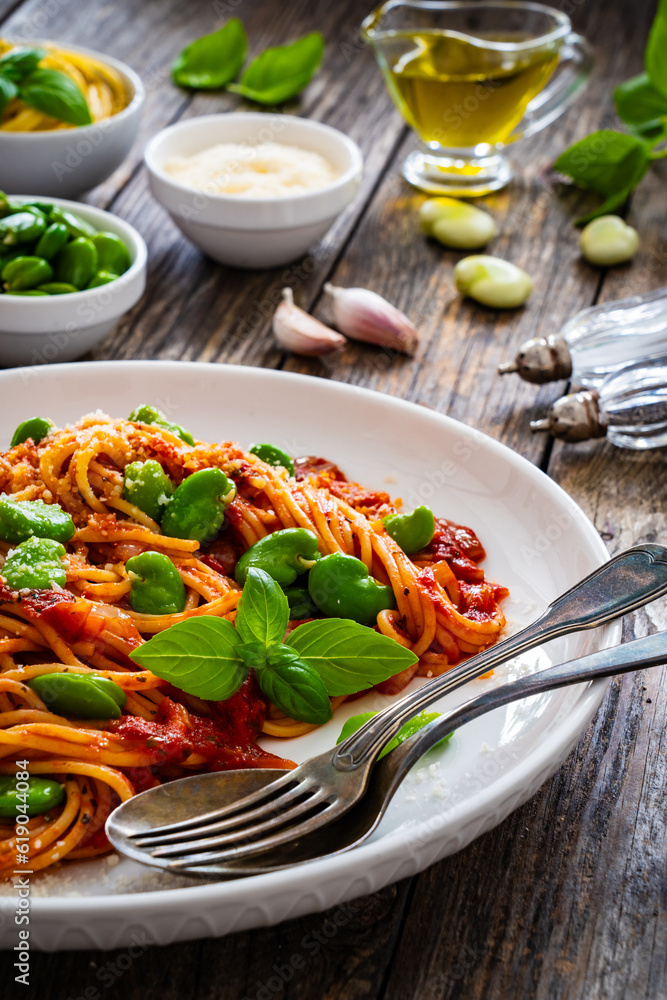Spaghetti in tomato sauce with broad bean, parmesan cheese and basil leaves on wooden table