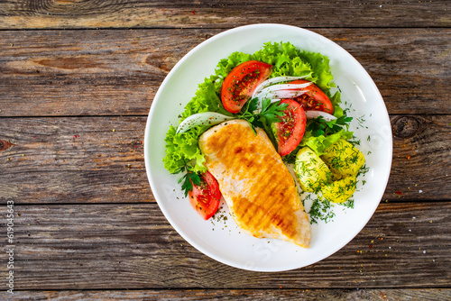Grilled chicken breast, boiled potatoes and fresh vegetables on wooden table
