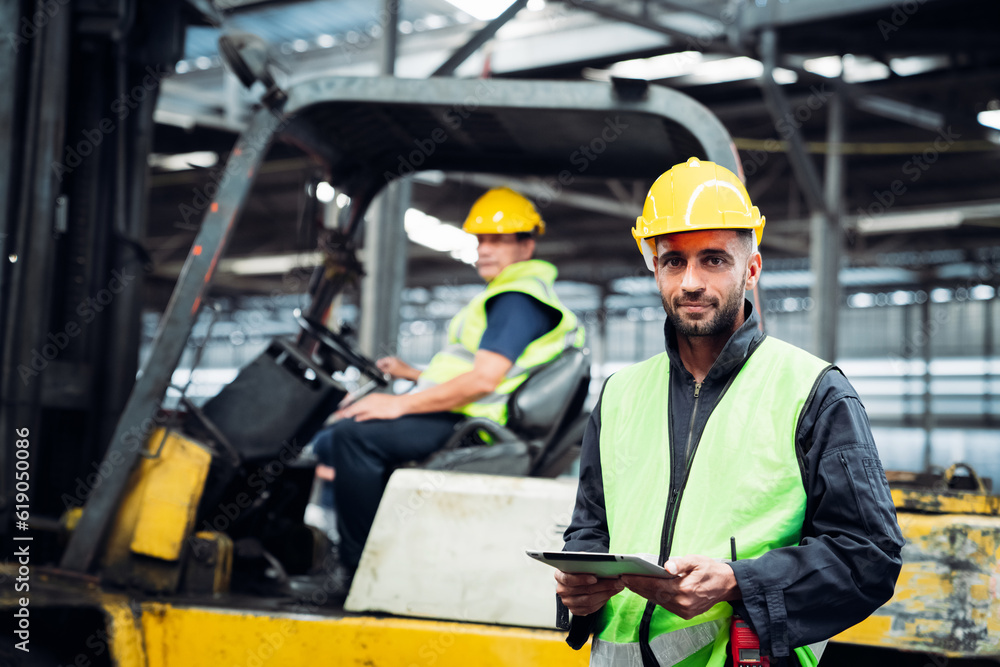 Industrial worker driving a forklift in the factory. Efficient Logistics Management and Teamwork in Manufacturing and Distribution Industry. Industrial worker driving a forklift in the factory. Efficient Logistics Management and Teamwork in Manufacturing and Distribution Industry.
