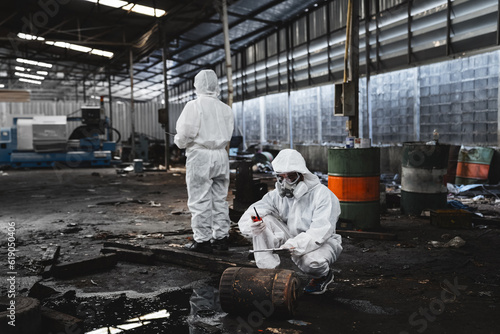 Scientist workers wear protection suit checking chemical contaminated oil in old factory. Protecting Against Hazards and Contamination. Emergency Response to a Radioactive Accident.