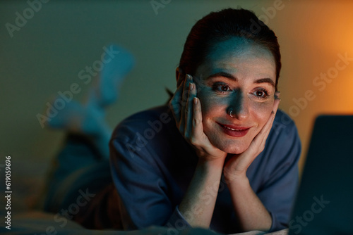 Foto Closeup portrait of young woman binge watching movies at night while lying on be