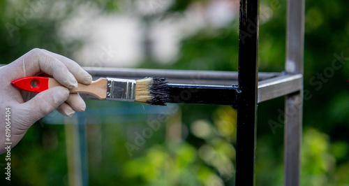 Fotografia a man paints metal with black paint with a brush.