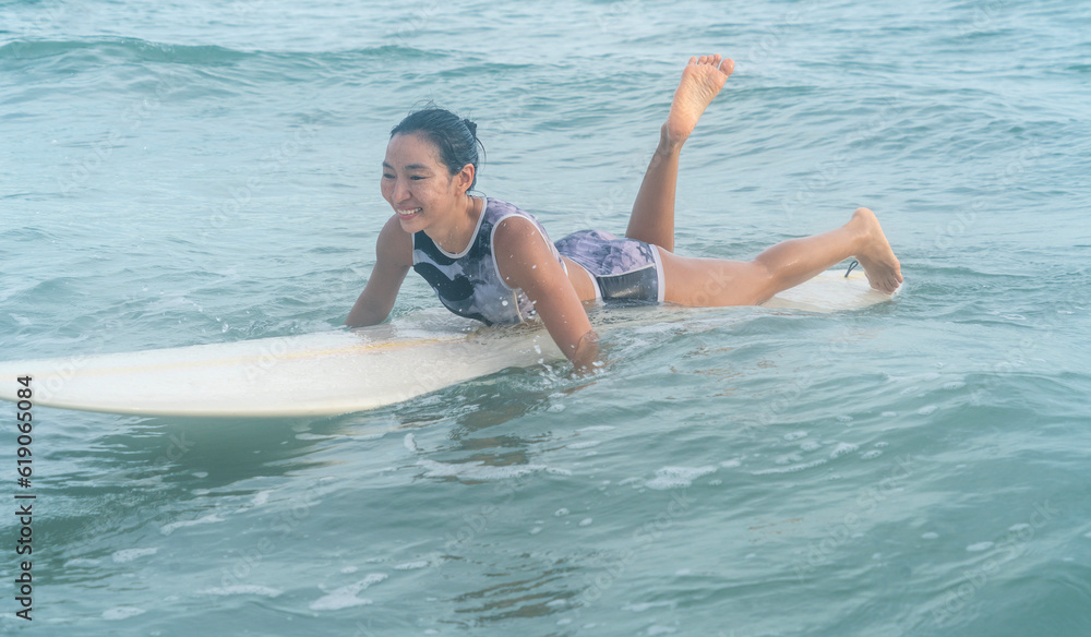 Asian girl sporting and surfing as a hobby, practicing surfing lie down and swim with a board in the sea Waiting for the big wave to stand on the board
