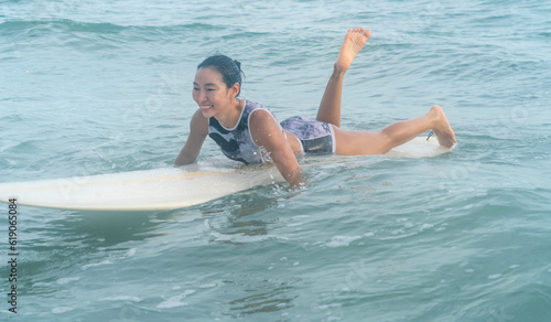 Asian girl sporting and surfing as a hobby, practicing surfing lie down and swim with a board in the sea Waiting for the big wave to stand on the board 