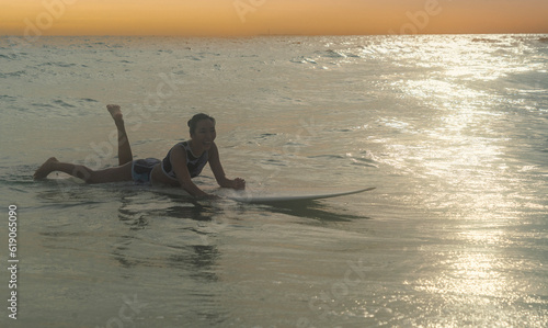 Asian girl sporting and surfing as a hobby, practicing surfing lie down and swim with a board in the sea Waiting for the big wave to stand on the board until the sun goes down
