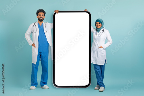 Arab doctor woman and man in uniform standing near big blank smartphone