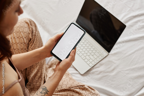 Minimal top view at young woman using laptop and smartphone with blank white screen on bed, copy space