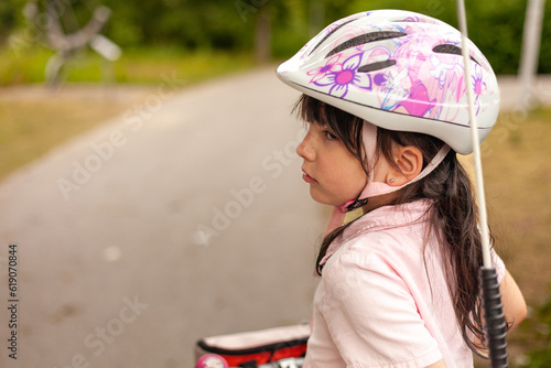 Little dark-haired girl cyclist in a bicycle helmet and a pink dress on a bicycle path © PeterPike
