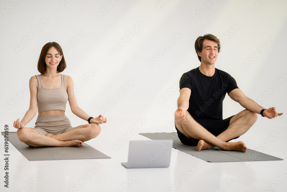 Smiling young european guy and lady in sportswear meditating, practice yoga on mat with laptop Smiling young european guy and lady in sportswear meditating, practice yoga on mat with laptop