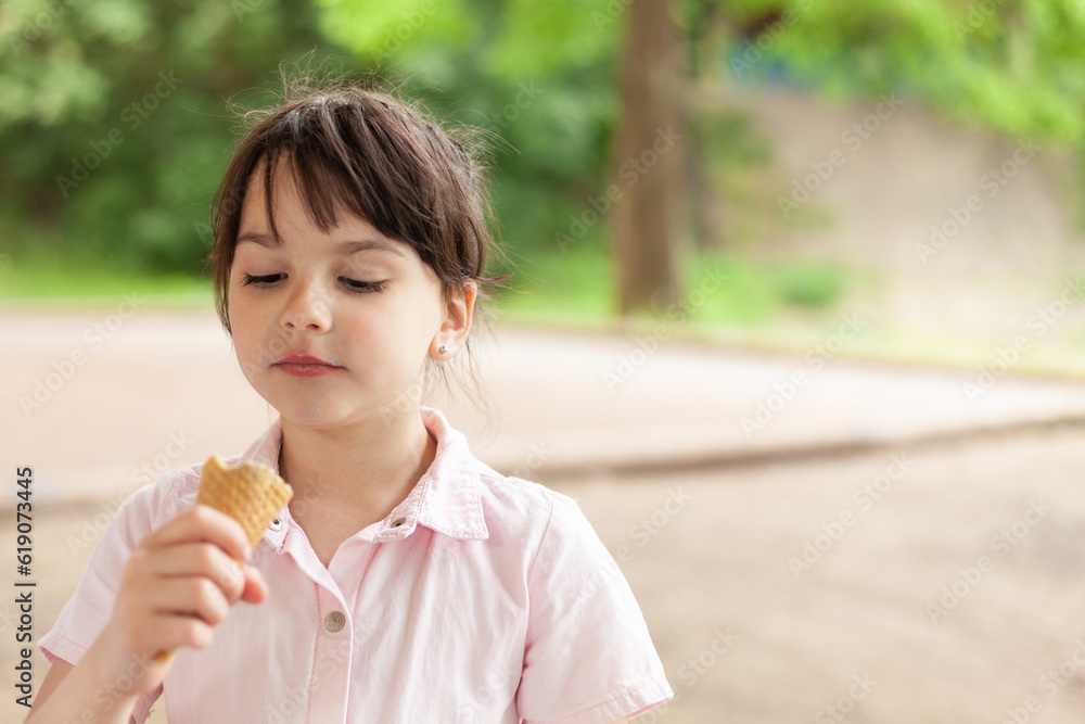 Little beautiful dark-haired girl in a dress eats an ice cream cone in the park Little beautiful dark-haired girl in a dress eats an ice cream cone in the park