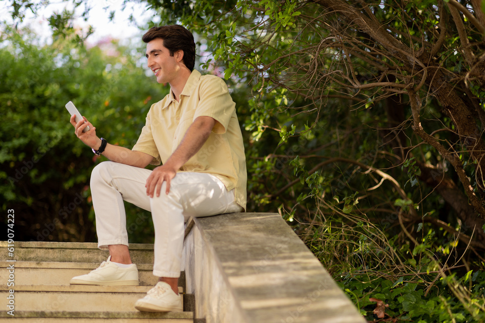 Fototapeta premium relaxed handsome guy sitting on stairs outdoors, using phone