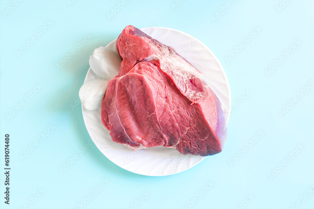 A piece of raw red meat with onion slices on a white plate on a light background close-up A piece of raw red meat with onion slices on a white plate on a light background close-up