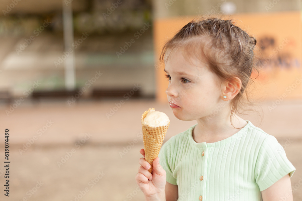 Little blonde girl in a dress eats an ice cream cone outdoors Little blonde girl in a dress eats an ice cream cone outdoors