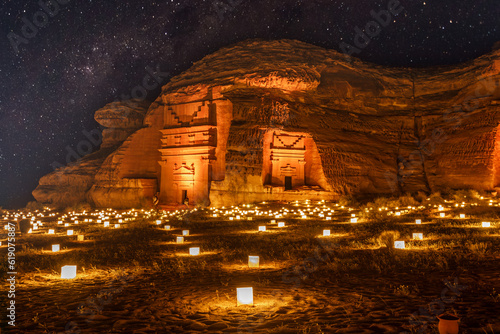 Starlight sky over the ancient nabataean tombs of Mada'in Salih Hegra city illuminated, night panorama, Al Ula, Saudi Arabia