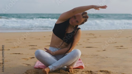 Female boxer MMA fighter girl doing seated side bend on beach at sunset sunrise. photo