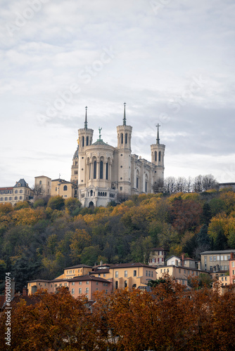 A stunning view of Lyon, France captured from the river, showcasing the iconic Basilica of Notre-Dame de Fourvière perched atop the hill. A beautiful scene that captures the essence of this historic c