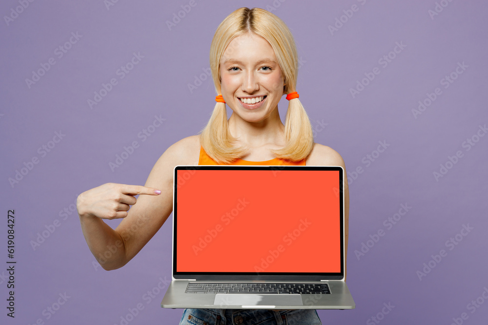 Happy young blonde IT woman wears orange tank shirt casual clothes hold use work point on laptop pc computer with blank screen workspace area isolated on plain pastel light purple background studio. Happy young blonde IT woman wears orange tank shirt casual clothes hold use work point on laptop pc computer with blank screen workspace area isolated on plain pastel light purple background studio.