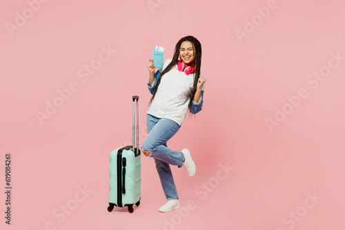 Traveler woman wear casual clothes hold suitcase passport ticket do winner gesture isolated on plain background. Tourist travel abroad in free spare time rest getaway. Air flight trip journey concept.