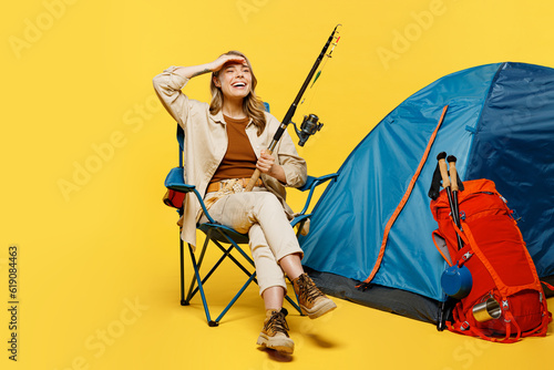 Full body happy young woman sit near bag with stuff tent hold fishing rod isolated on plain yellow background. Tourist leads active lifestyle walk on spare time. Hiking trek rest travel trip concept. #619084463