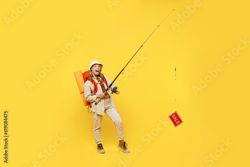 Full body young woman carry bag stuff mat holding fishing rod with sale text isolated on plain yellow background Tourist leads active lifestyle walk on spare time. Hiking trek rest travel trip concept