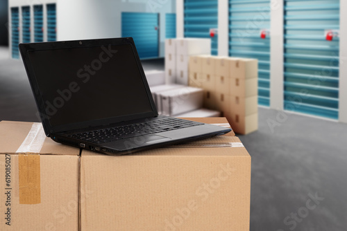 Warehouse business. Laptop on boxes. Parcel near storage units. Warehouse corridors. Doors to storage containers. Laptop for renting warehouse via internet. Boxes near storage units. 3d image © Grispb