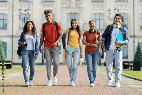 Happy university students walking together on campus, laughing and looking at camera