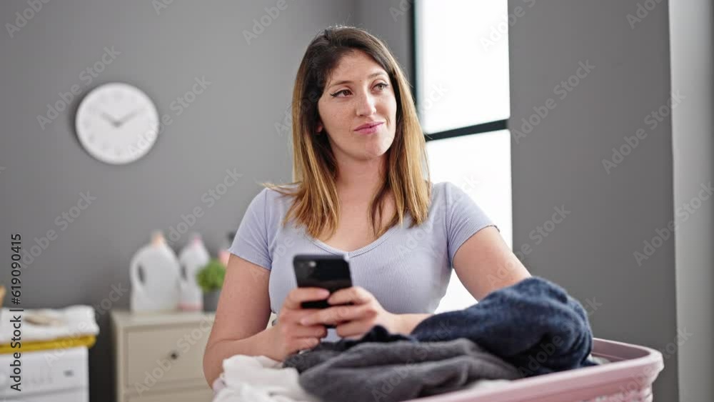 Young blonde woman using smartphone hanging clothes on clothesline at laundry room Young blonde woman using smartphone hanging clothes on clothesline at laundry room