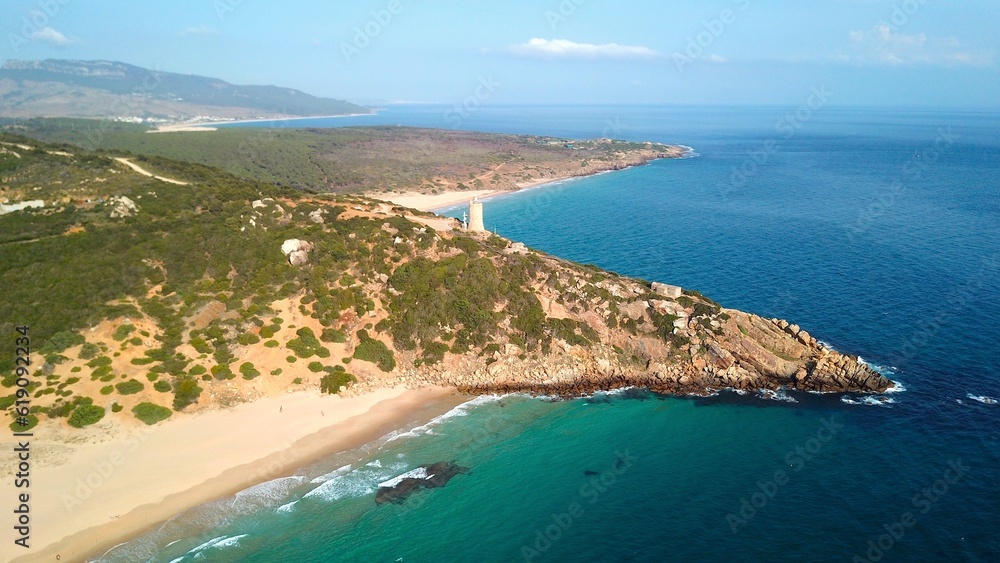 Faro de Camarinal, aerial view of the lighthouse on a cliff at the wonderful sandy beach with the blue turquoise Atlantic Ocean, Playa Los Alemanes, Andalusia, Spain