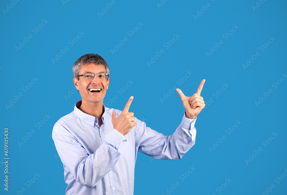 Excited Mature Man Pointing Fingers Aside Posing Over Blue Background Excited Mature Man Pointing Fingers Aside Posing Over Blue Background