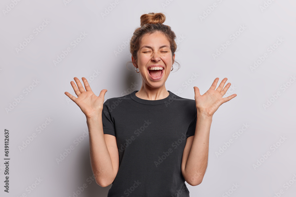 Waist up shot of positive cheerful woman raises her palms and exclaims loudly responding to wonderful gift or surprise dressed in casual black t shirt isolated over white background. Human reactions Waist up shot of positive cheerful woman raises her palms and exclaims loudly responding to wonderful gift or surprise dressed in casual black t shirt isolated over white background. Human reactions