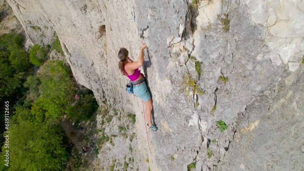 CLOSE UP: Young lady clipping in belay rope while lead climbing in limestone wall. She advances effortlessly and moves quickly on a sharp end of rope at incredible climbing area in Karst landscape. CLOSE UP: Young lady clipping in belay rope while lead climbing in limestone wall. She advances effortlessly and moves quickly on a sharp end of rope at incredible climbing area in Karst landscape.