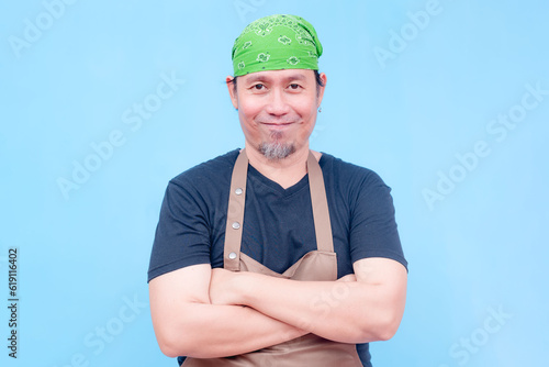 A smiling middle-aged barista wearing brown apron standing straight with arms across chest. Isolated on a blue background.