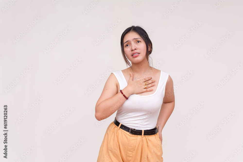 A sad and disappointed young Asian woman holding her chest in frustration. Isolated on a white background. A sad and disappointed young Asian woman holding her chest in frustration. Isolated on a white background.
