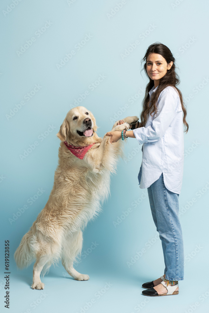 Beautiful golden labrador standing on hind legs, being held by cute Latin woman looking at camera