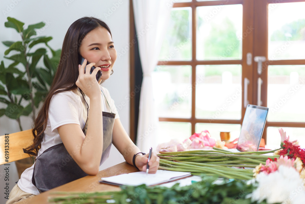 Flower shop concept, Female florist talking with customer on smartphone and taking note on notebook Flower shop concept, Female florist talking with customer on smartphone and taking note on notebook