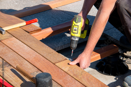 Wood worker with a power screwdriver and carpenter tools installing a deck, hardwood decking