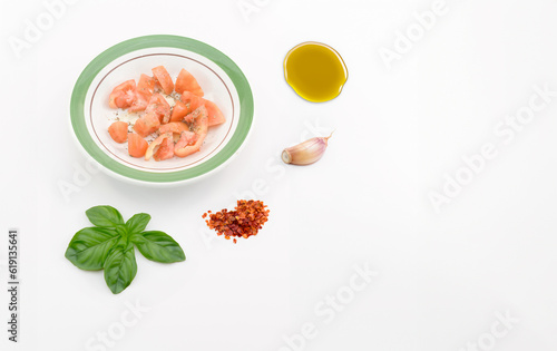 illustrazione Generative Ai con piatto di pomodori a tocchetti conditi con olio e origano, superficie bianca con basilico foglie, aglio spicchio, olio e peperoncino